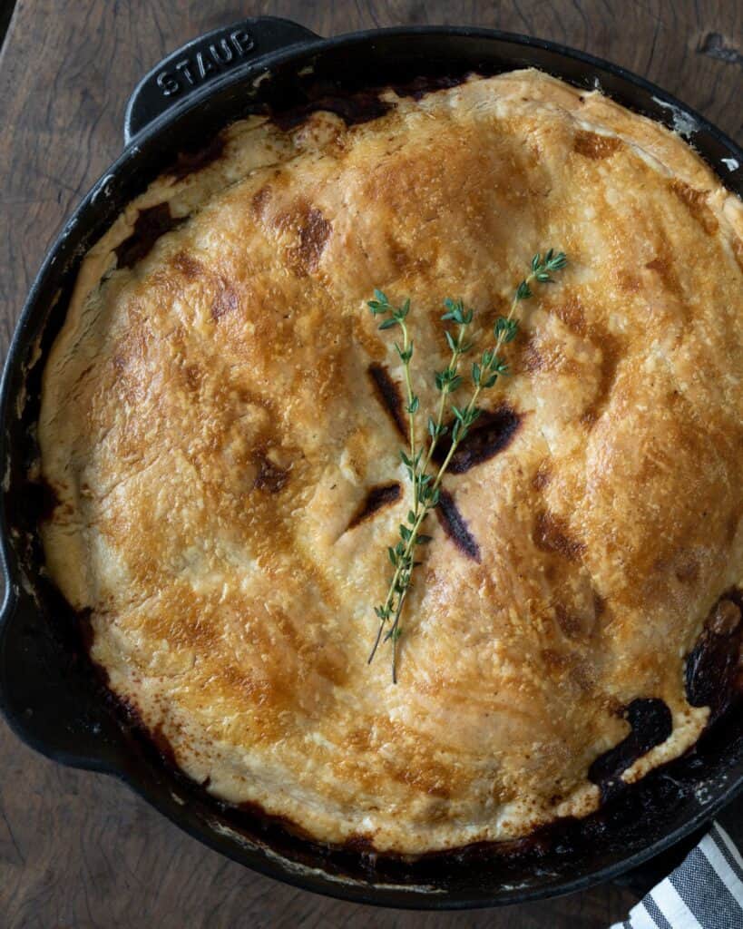 pot pie in a staub cast iron skillet with thyme sprigs on top