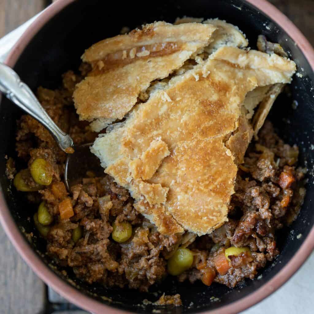 slice of ground beef pot pie in a bowl with a silver spoon