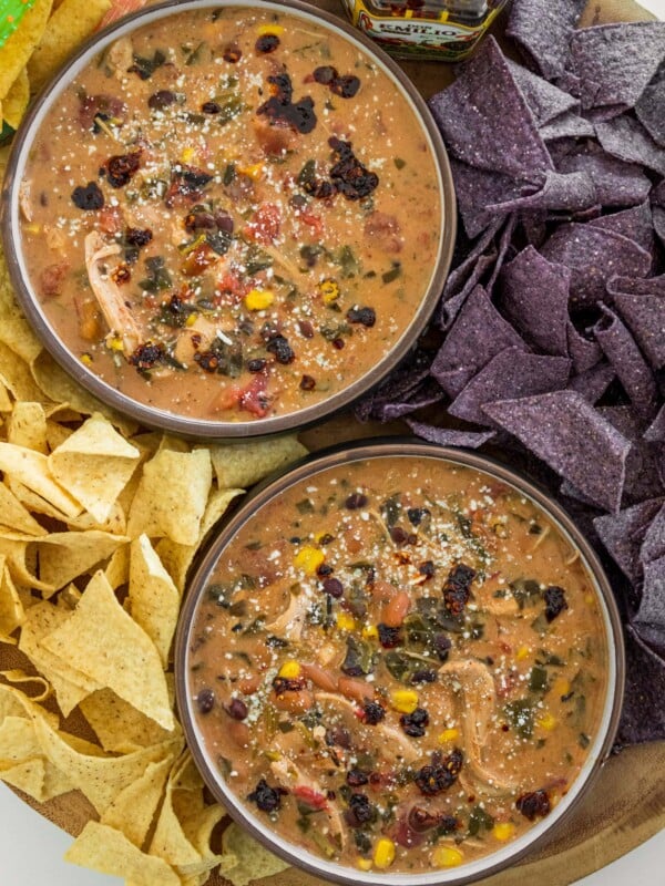 bowls of chicken taco soup garnished with cotija cheese and salsa macha surrounded by blue corn and white corn tortilla chips