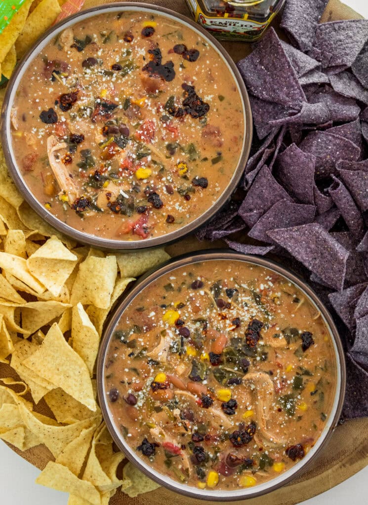 bowls of chicken taco soup garnished with cotija cheese and salsa macha surrounded by blue corn and white corn tortilla chips