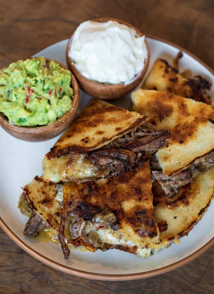 beef quesadillas on a plate with sides of sour cream and guacamole