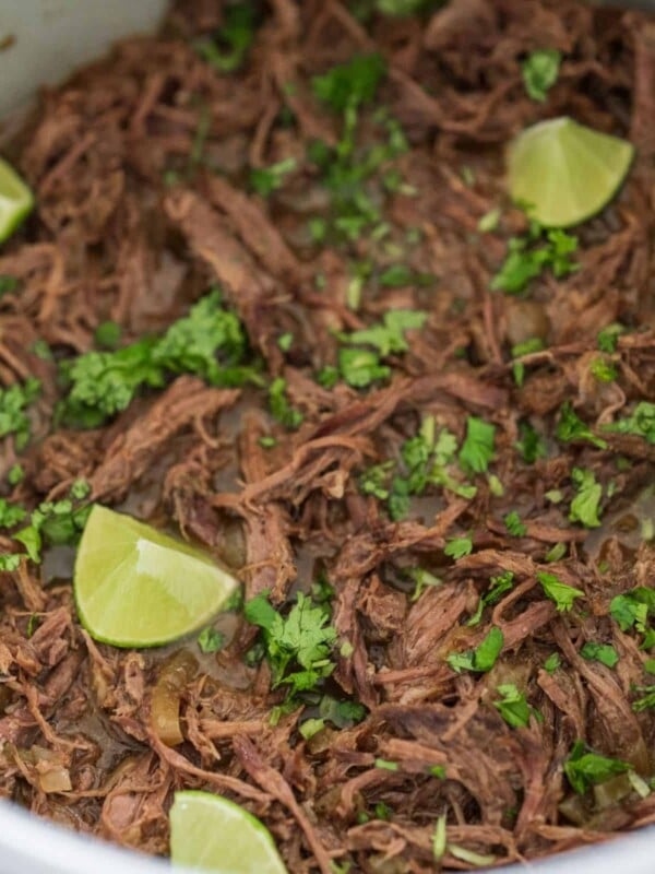 pulled beef shoulder roast in a slow cooker with fresh cilantro and lime wedges