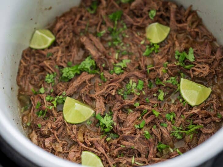 pulled beef shoulder roast in a slow cooker with fresh cilantro and lime wedges