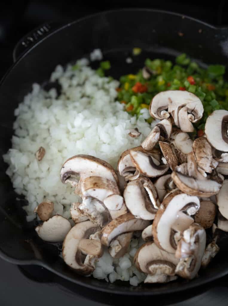 sliced mushrooms in a skillet with diced onion and bell pepper