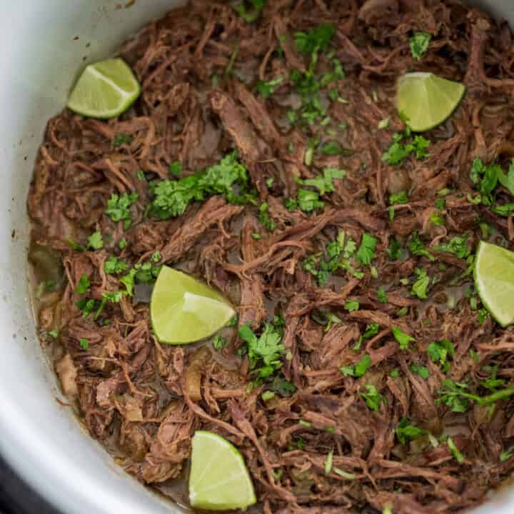 shredded slow cooked beef shoulder roast with lime wedges and fresh cilantro
