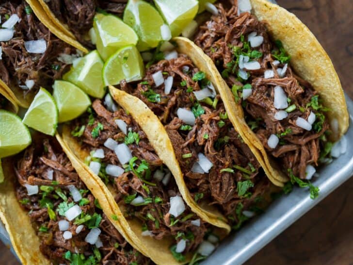 Mexican shredded beef tacos garnished with diced onion, chopped cilantro, and lime wedges