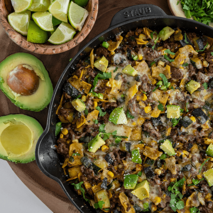 beef enchilada skillet with a halved avocado, lime wedges, cotija cheese, and chopped cilantro