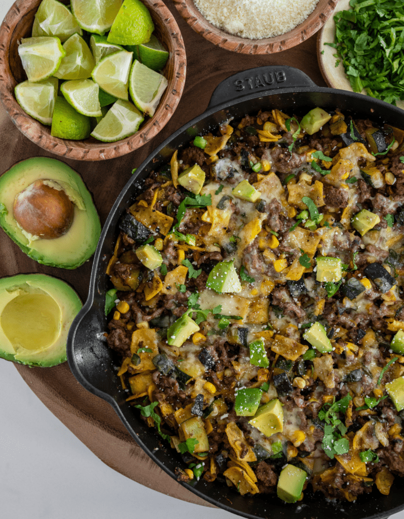 beef enchilada skillet with a halved avocado, lime wedges, cotija cheese, and chopped cilantro