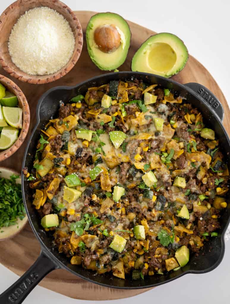 finished beef enchilada skillet with cotija cheese, limes, avocado, and cilantro