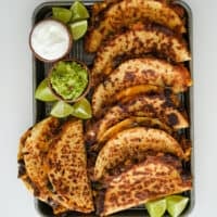 southwest ground beef quesadillas on a sheet pan with limes, guacamole, and Greek yogurt
