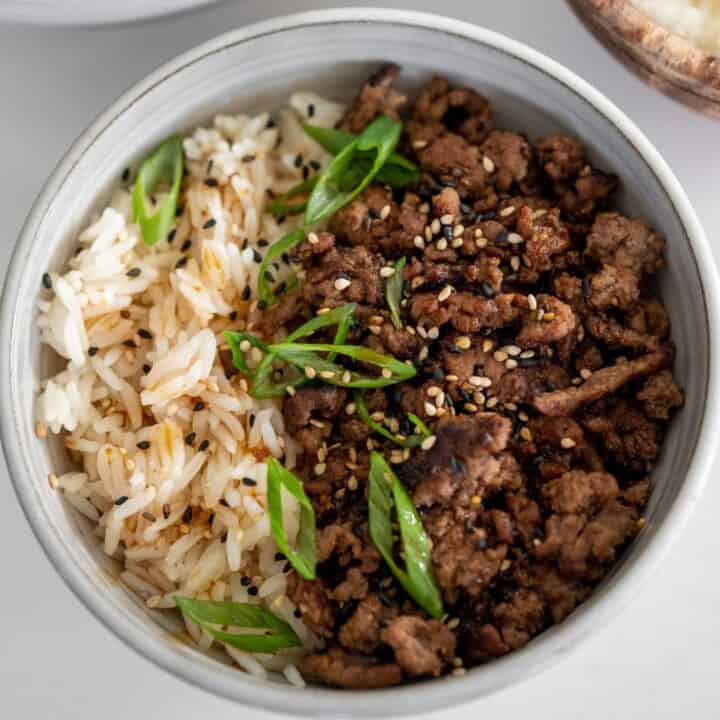 black pepper ground beef and rice in a bowl topped with scallions and sesame seeds
