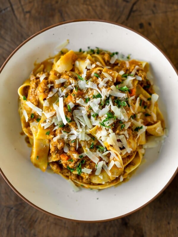 bowl of pumpkin bolognese with pasta, fresh herbs, and grated parmesan