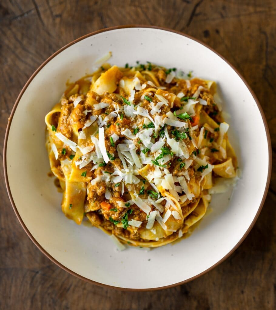 bowl of pumpkin bolognese with pasta, fresh herbs, and grated parmesan