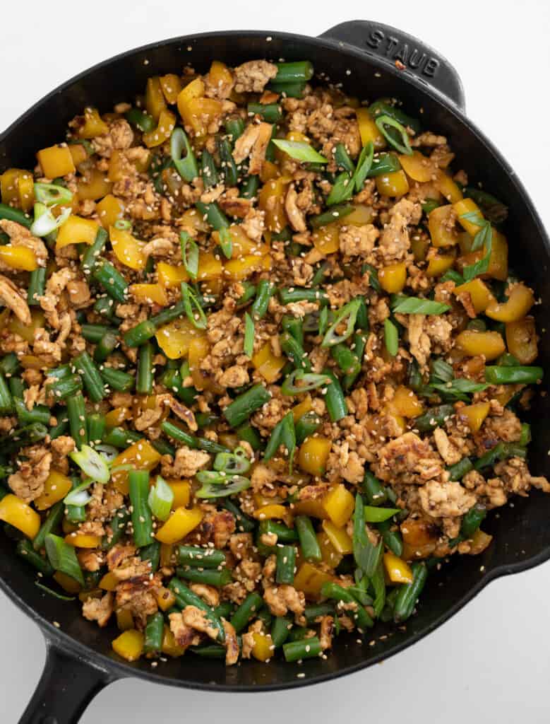 honey sesame ground chicken, bell peppers, and green beans in a cast iron skillet