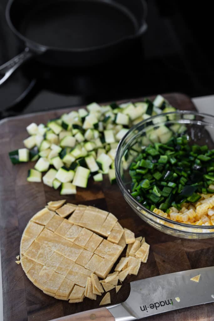 chopped corn tortillas on a cutting board with diced poblano, zucchini, and corn