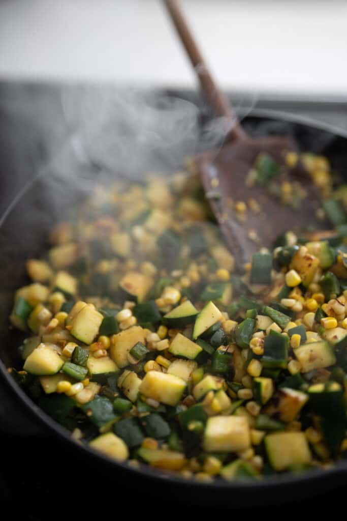 cooking zucchini, corn, and poblano peppers in a cast iron skillet