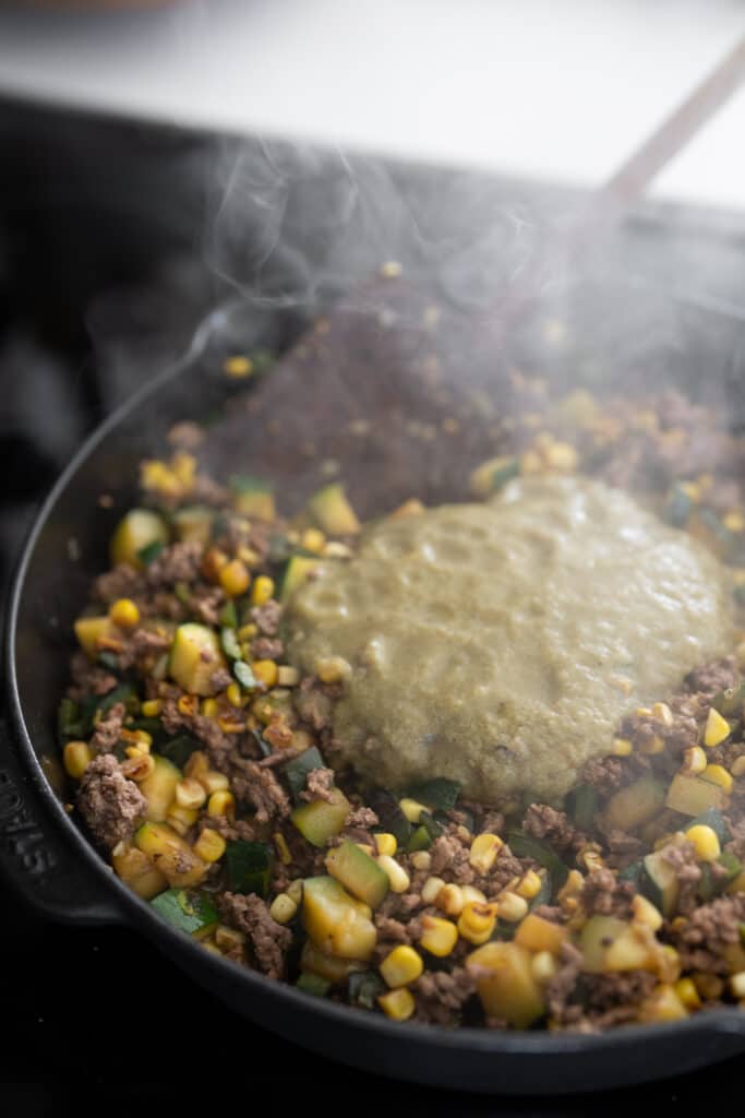 green chile enchilada sauce in the skillet with the cooked ground beef and veggies