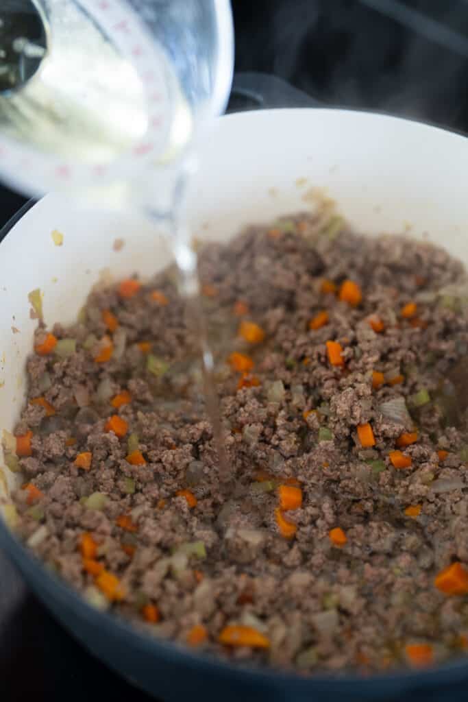 adding wine to cooked ground beef and mirepoix in a Dutch oven