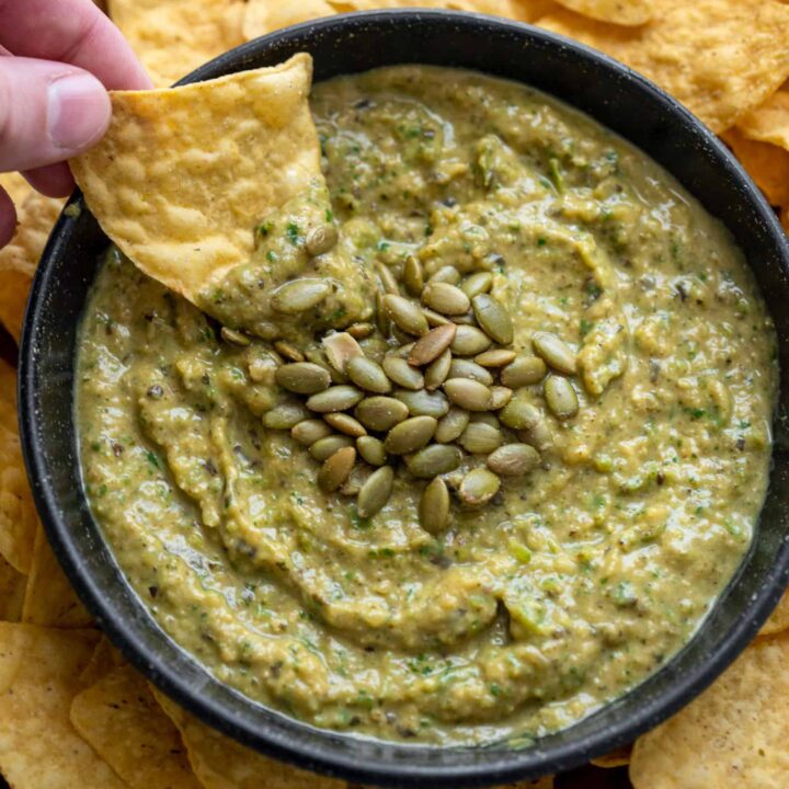 dipping a tortilla chip in zucchini salsa topped with pepitas