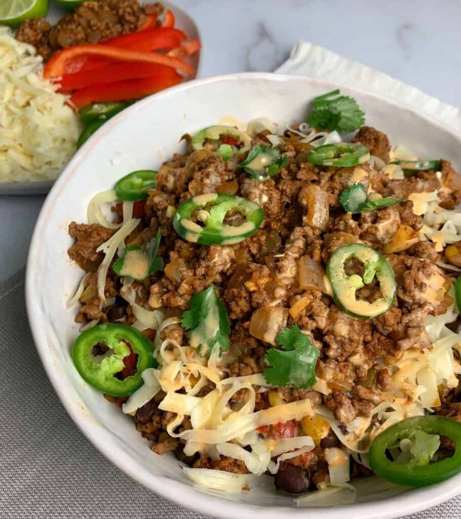 taco beef and rice bowls garnished with jalapeño slices, yogurt sauce, and shredded cheese