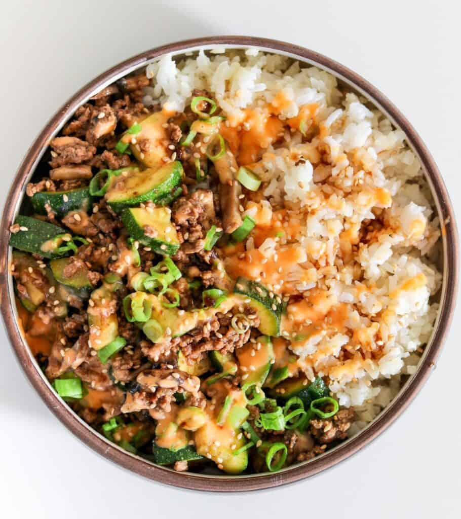 power bowl with teriyaki ground beef and veggies with rice, cauliflower rice, yum yum sauce, sesame seeds, and scallions