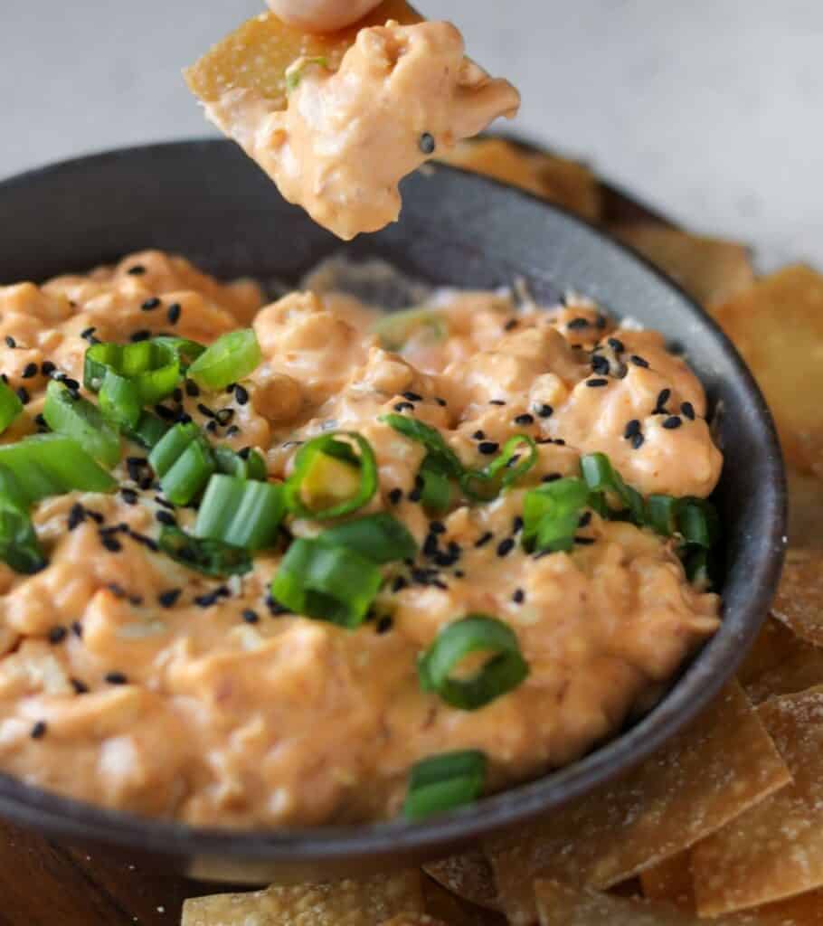 baked wonton chips with a bowl of chicken dip garnished with scallions and sesame seeds