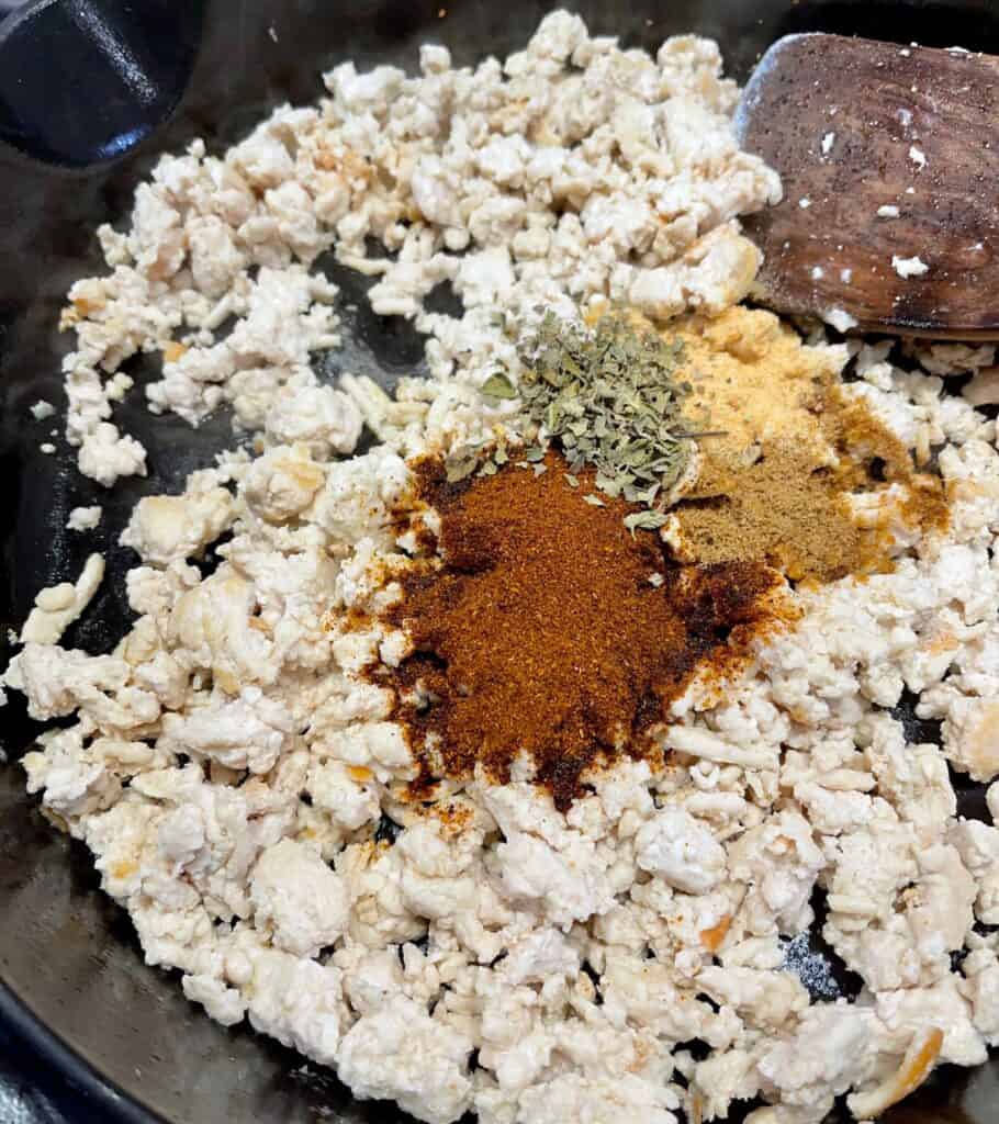 cooked ground chicken in a cast iron skillet with chili powder, garlic powder, oregano, and ground cumin