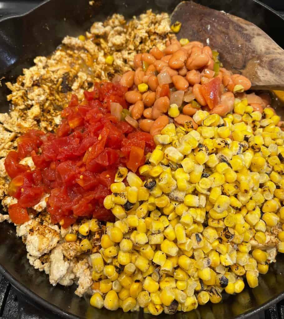 roasted corn, canned beans, and RO-TEL in a cast iron skillet with seasoned ground chicken