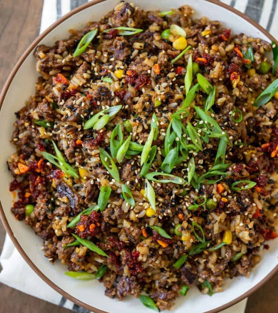 bowl of ground beef fried rice garnished with sliced scallions and sesame seeds