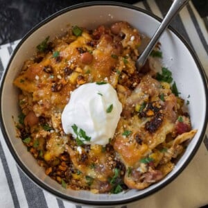 serving of ground chicken taco casserole in a white bowl garnished with salsa macha, cilantro, and nonfat Greek yogurt