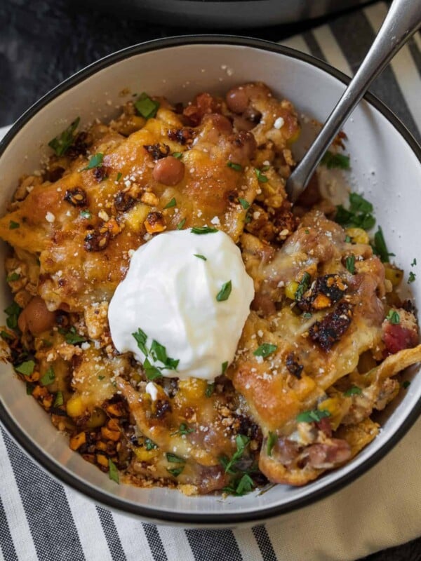 serving of ground chicken taco casserole in a white bowl garnished with salsa macha, cilantro, and nonfat Greek yogurt