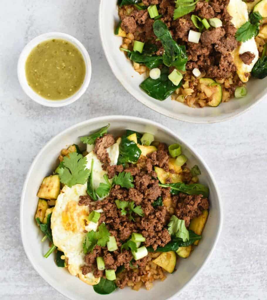 two beef bowls with fried eggs and a small bowl of salsa verde on the side