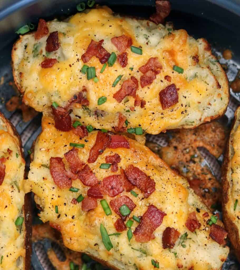 two twice baked potatoes with chopped bacon and chives in an air fryer basket
