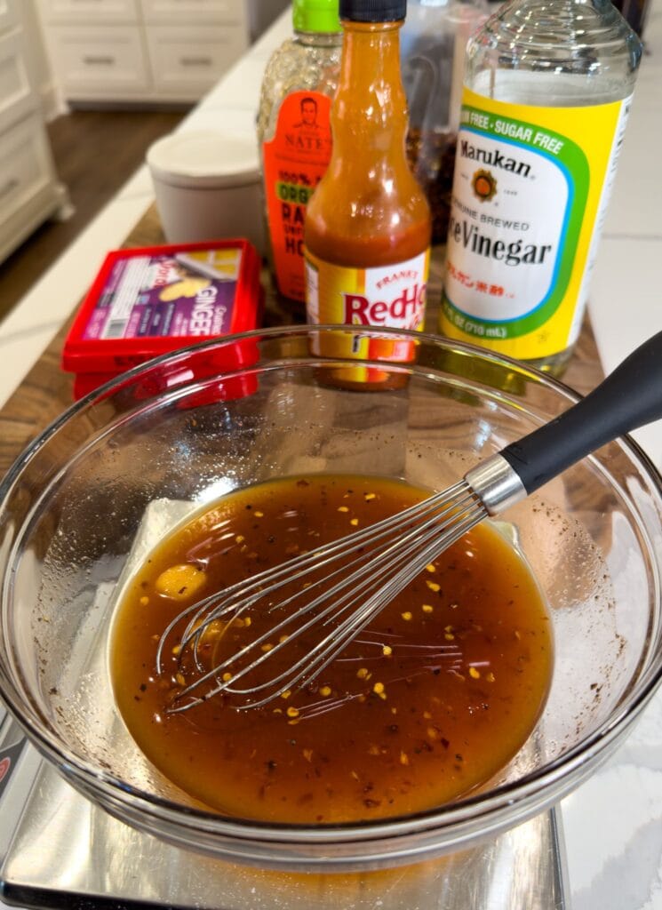 making firecracker sauce in a bowl with a whisk and ingredients behind it on a cutting board