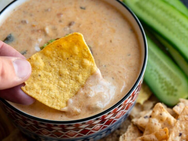 dipping a tortilla chip in a bowl of protein queso