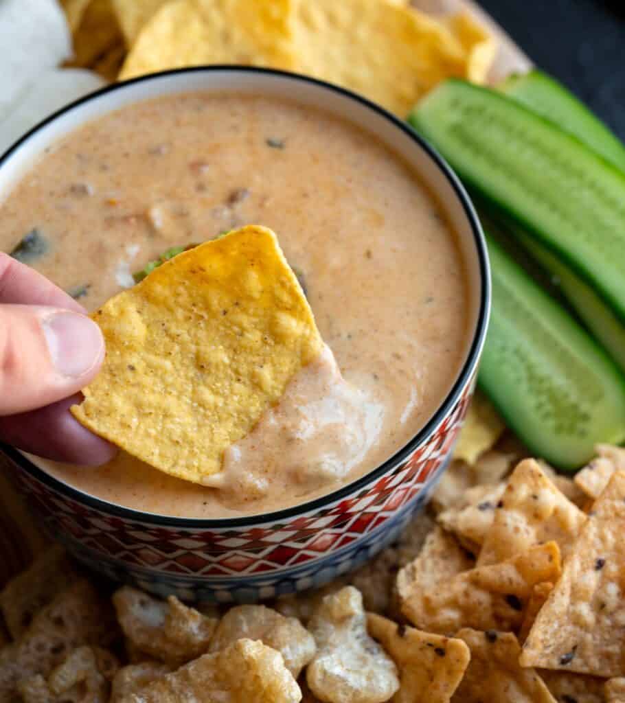 dipping a tortilla chip in a bowl of protein queso