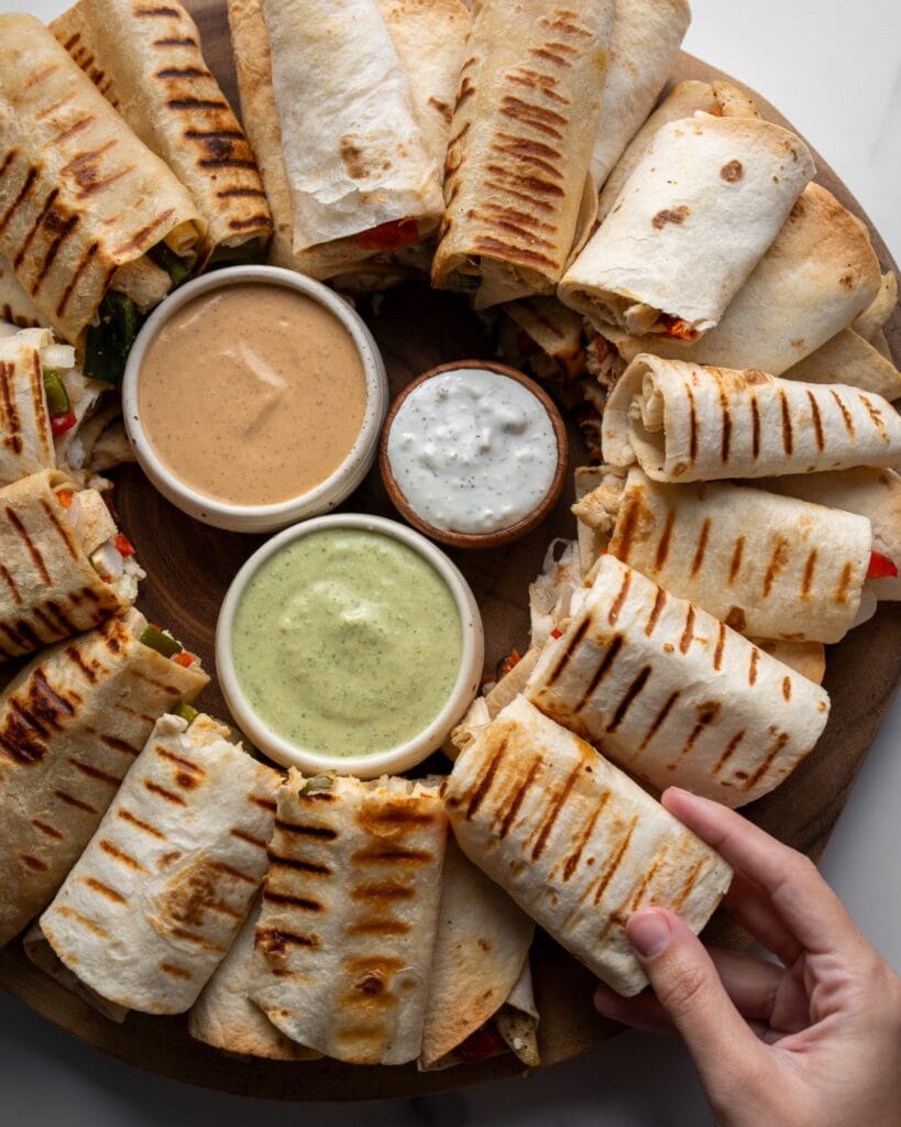 grabbing a grilled chicken breast wrap from a tray with a circle of chicken wraps around a dip trio