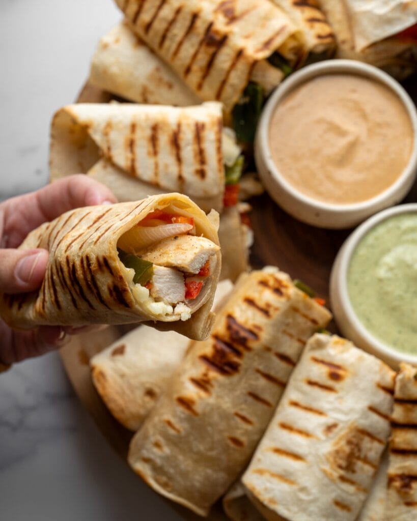 holding a chicken breast wrap above a serving board with dips