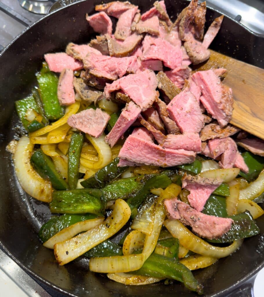 cooked peppers and onions in a skillet with sliced sirloin