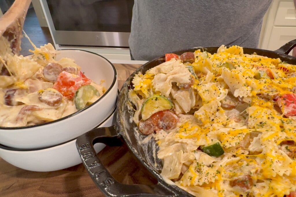 serving a cajun chicken sausage pasta skillet into two bowls with a wooden spoon