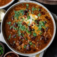 bowl of high protein turkey chili with chopped cilantro, nonfat Greek yogurt, shredded cheese, and salsa macha