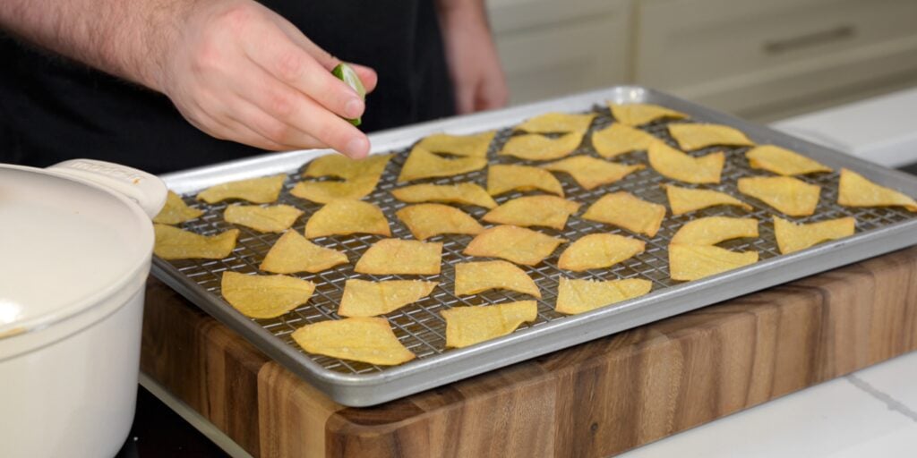 squeezing a lime wedge over baked tortilla chips on a sheet pan