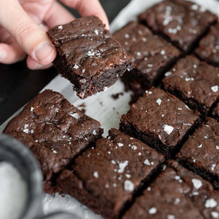 holding a brownie square over parchment paper with flaky salt on top