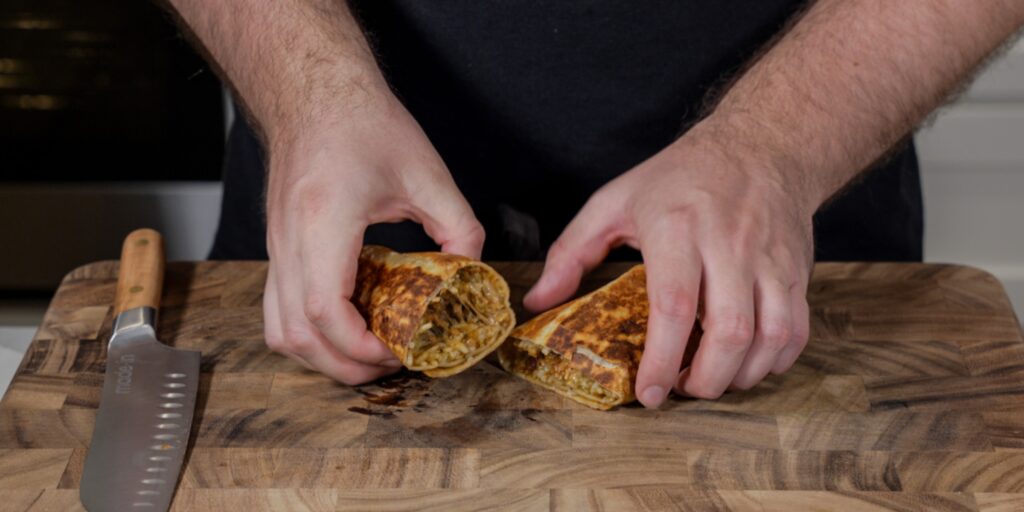 slicing a chili cheese burrito in half on a cutting board