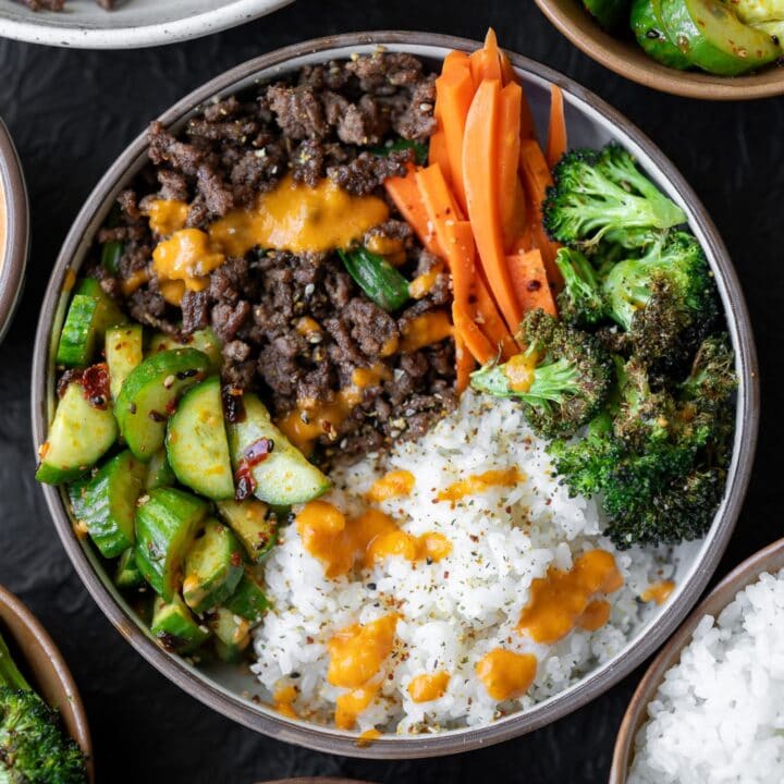 ground beef bulgogi bowl with kimchi sauce, sticky rice, sesame seeds, roasted broccoli, cucumber salad, and pickled carrots