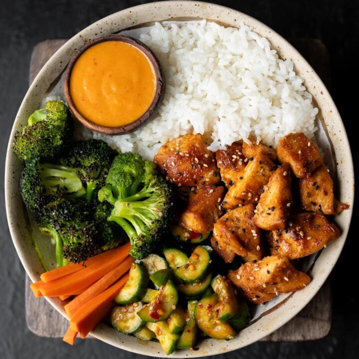 roasted chicken and broccoli in a bowl with sticky rice, kimchi sauce, cucumber salad, and pickled carrots