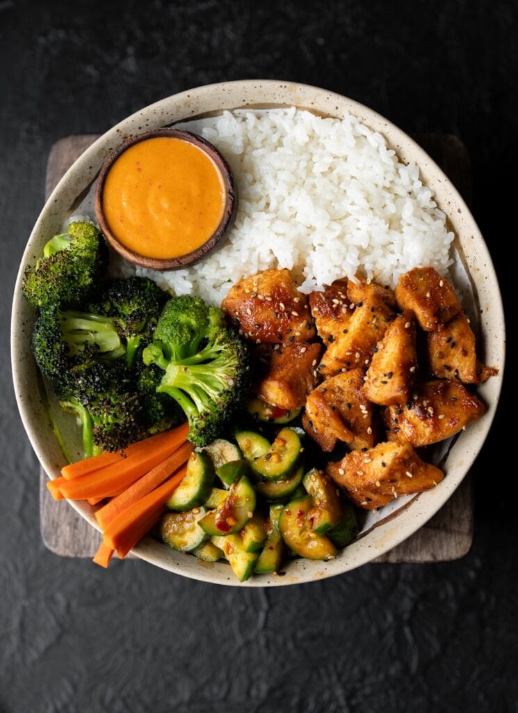 sheet pan roasted chicken and broccoli in a bowl with sticky rice, pickled carrots, cucumber crunch salad, and creamy kimchi sauce