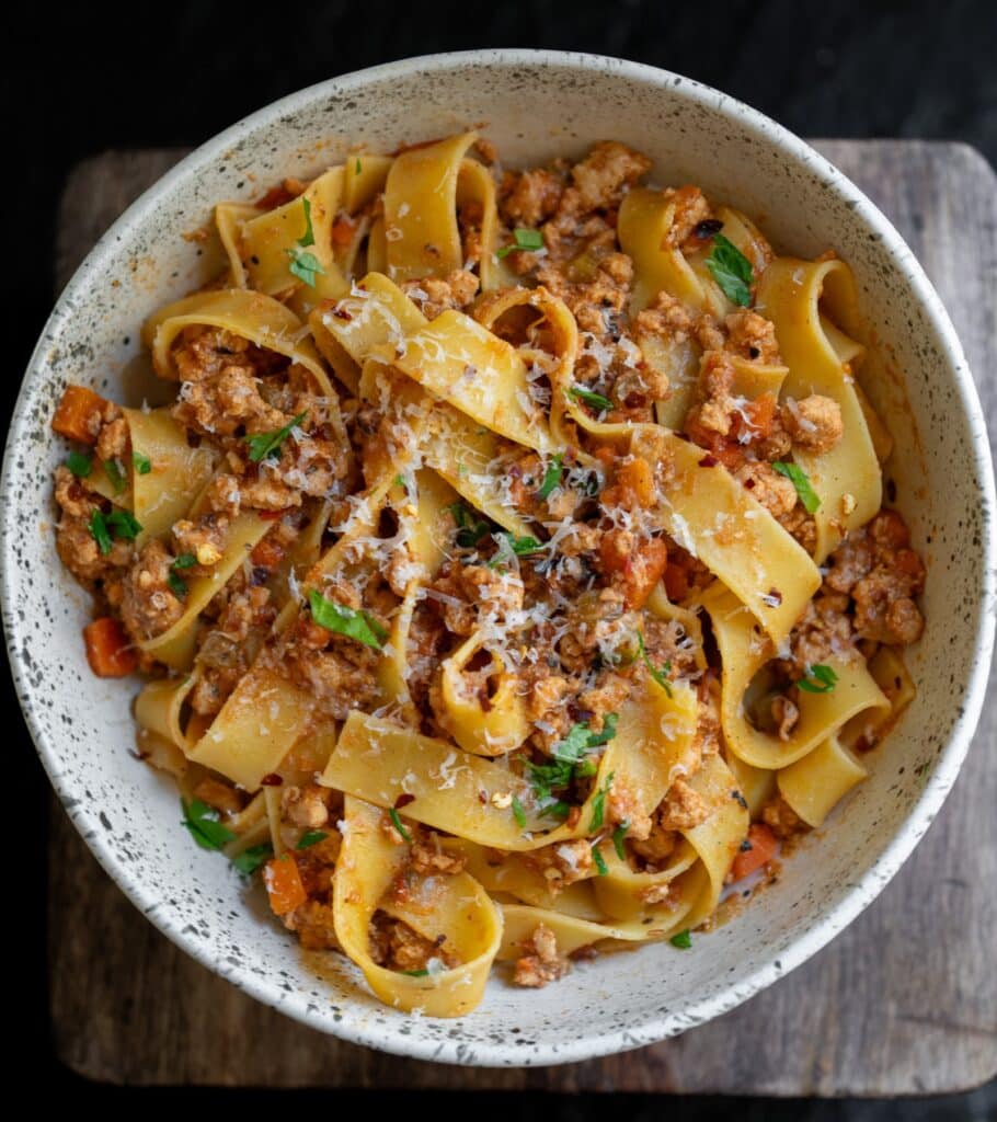ground turkey bolognese pasta in a bowl garnished with parsley and parmigiano reggiano