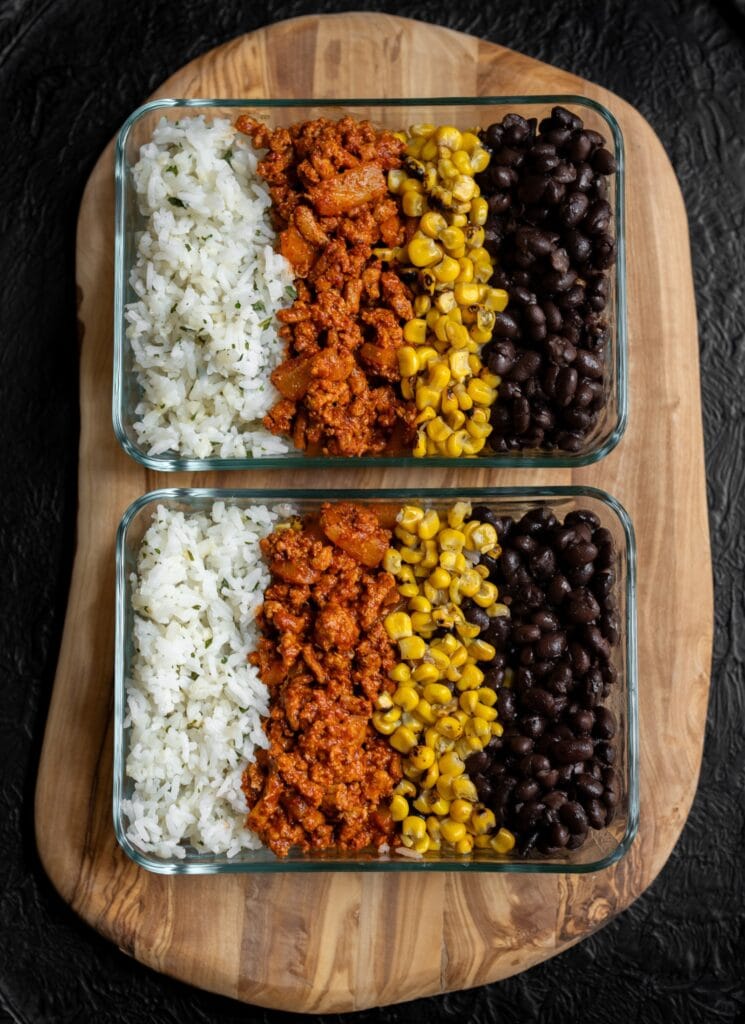 two meal prep containers with half calorie rice, al pastor ground turkey, fire roasted corn, and black beans