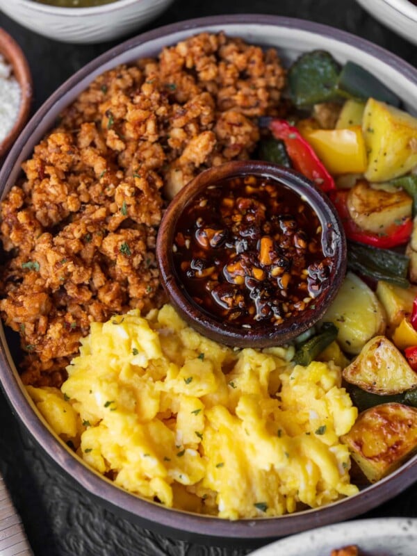 breakfast bowl with scrambled egg, sweet and spicy ground chicken, roasted potatoes and peppers, and a small bowl of salsa macha